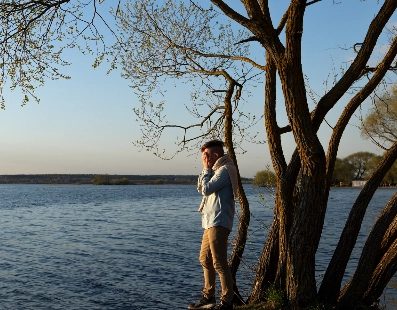 Man standing near a tree on a riverbank at sunset