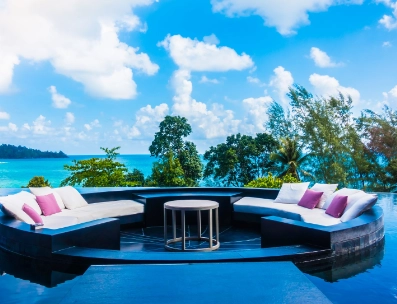 Outdoor circular seating with white cushions by a pool overlooking tropical trees and ocean